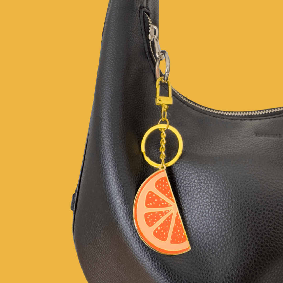 Black leather handbag with a keychain shaped like an orange slice on a yellow background