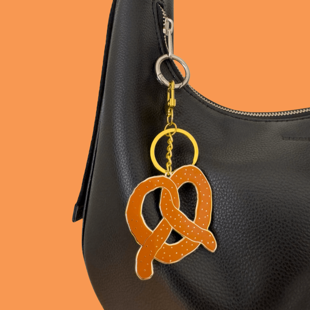 Black leather handbag with a pretzel-shaped keychain on an orange background