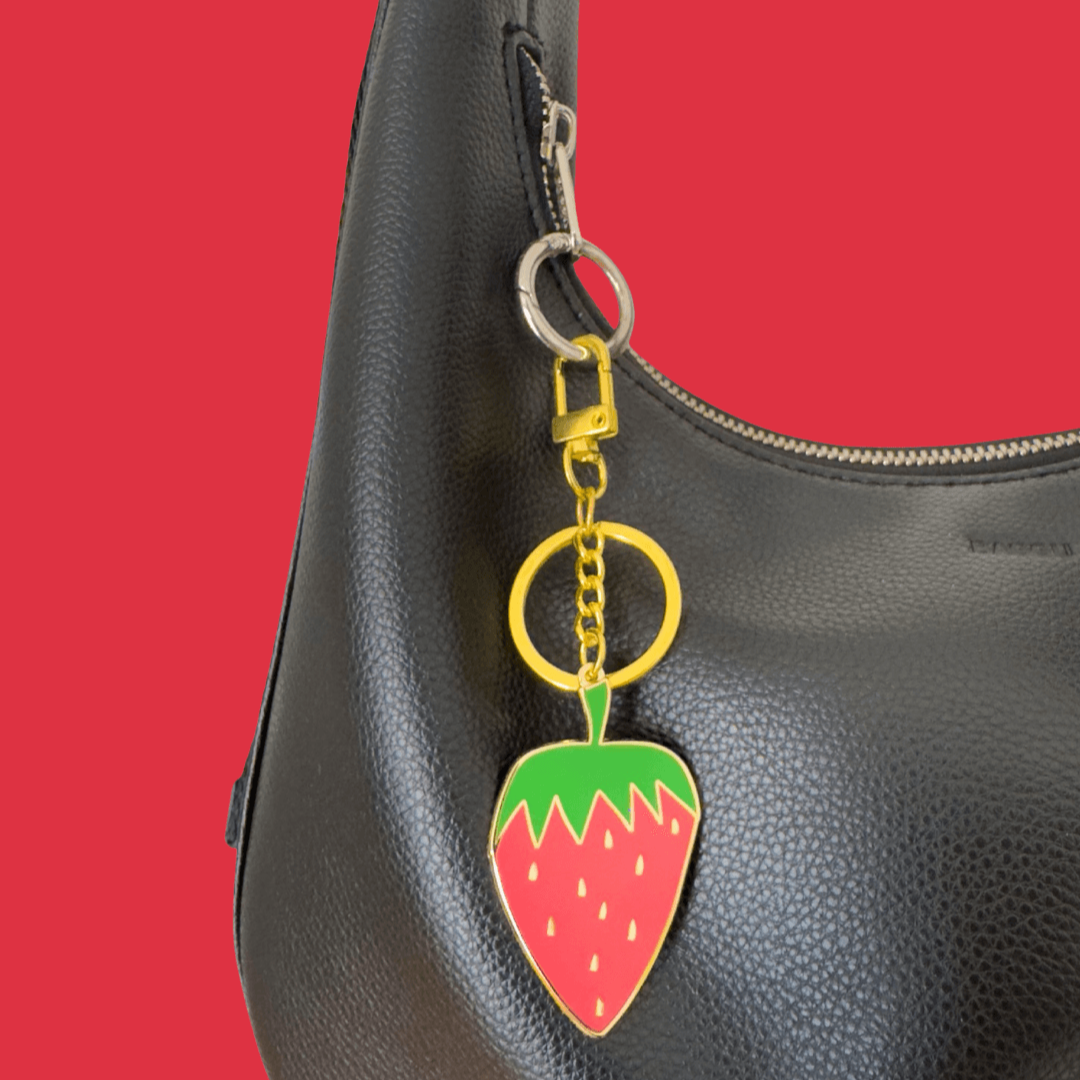 Black handbag with a strawberry-shaped keychain on a red background