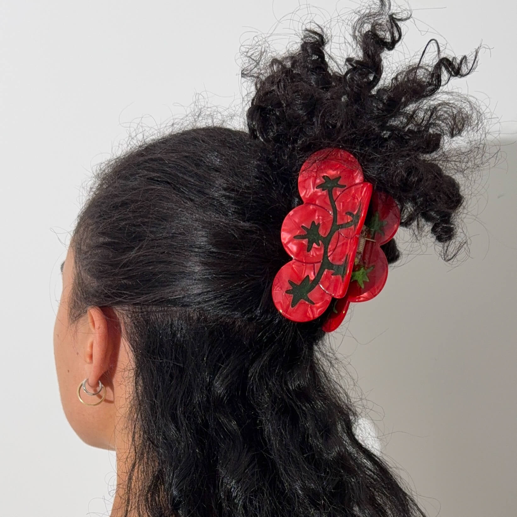 Person with black hair wearing a red tomato hair accessory against a white background