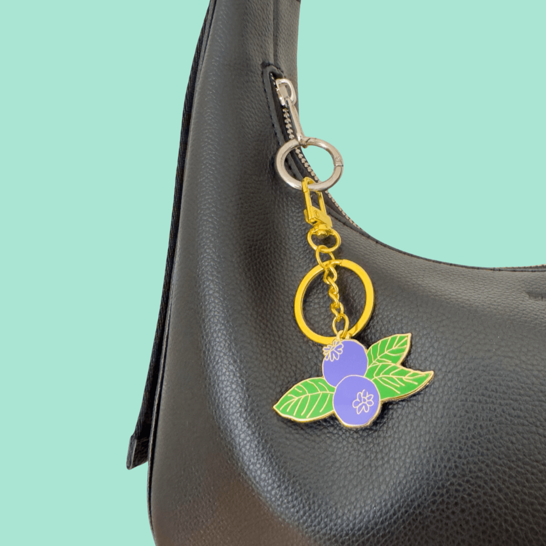 Keychain with blue and green design attached to a black bag on a teal background
