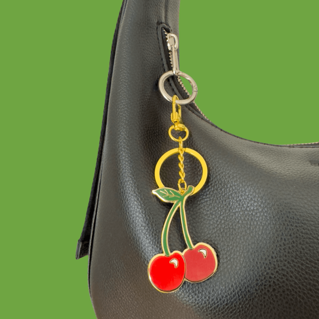 Cherry keychain attached to a black handbag on a green background
